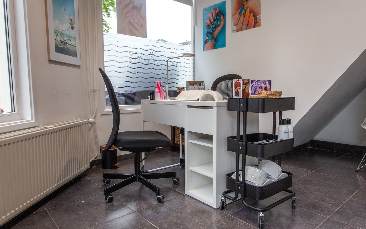 De nageltafel van Nails by Ais met bureaustoel, trolley en nagelposters aan de muur